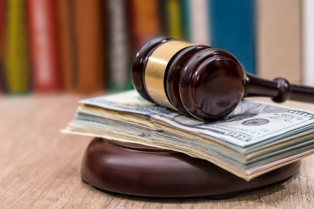 Judge gavel with dollars, books on  wooden desk close up.